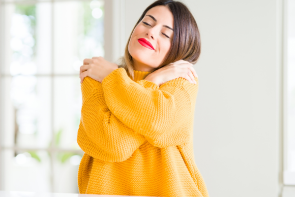 Women in yellow jumper hugging herself for why it is important to priorities yourself