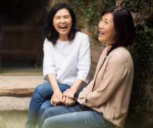 Two women with dark hair laughing and discussing why it is important to prioritise yourself